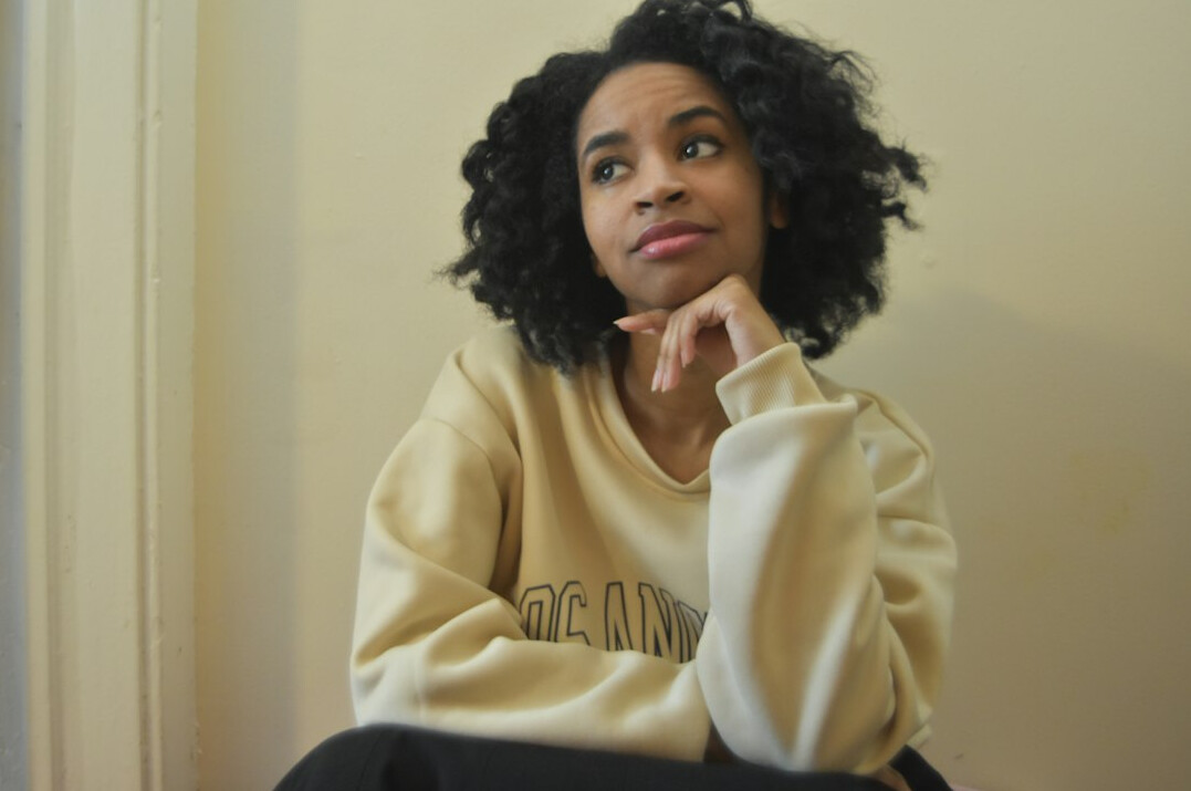 Portrait of a young woman with dark curly hair wearing a cream sweater against a neutral background